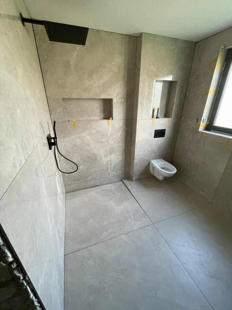 Bodengleiche Dusche mit großformatigen Fliesen in Marmoroptik und schwarzen Armaturen